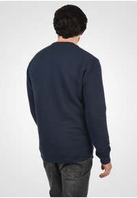Sudadera de cuello redondo en navy con textura acanalada, mangas largas y cintura ajustada, combinada con jeans grises.