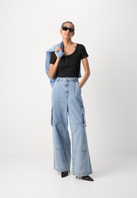 Top negru ajustat cu guler rotund, asortat cu pantaloni largi din denim bleumarin deschis, cu buzunare laterale. Ochelari de soare negri și o jachetă albastră.