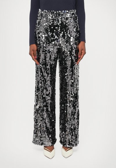 Pantaloni a paillettes con un motivo lucido in nero e argento, design a gamba larga e vita alta. Indossati con tacchi bianchi.