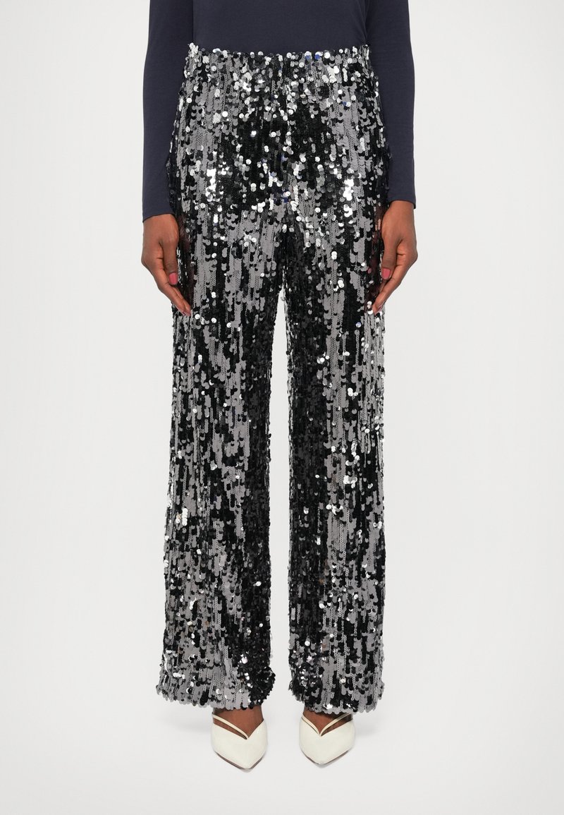 Pantaloni cu paiete, având un model strălucitor în alb și argintiu, design cu picioare largi și talie înaltă. Purtați cu pantofi cu toc albaștri.