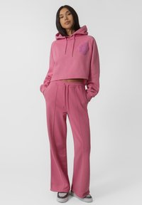 Haut de hoodie court rose avec un détail floral et des cordons de serrage, associé à un pantalon de jogging assorti à coupe ample avec poches latérales et accents de coutures.