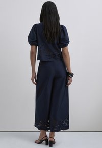 Conjunto de dos piezas azul marino que incluye un top corto con mangas abullonadas y detalles de encaje, combinado con pantalones de pierna ancha adornados con patrones florales.