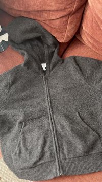 Szara bluza z zamkiem, wykonana z miękkiego materiału, z kapturem, dwoma przednimi kieszeniami i ściągaczem u dołu. Gładka faktura z minimalnymi detalami szwów.