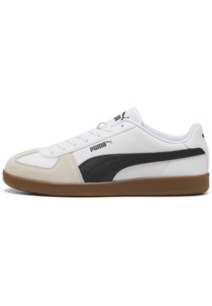 Witte Puma lage sneaker met zwarte strependetail, beige suède neus, witte veters en bruine rubberen zool.
