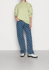 Ljusgrön huvtröja med en framficka, tillsammans med blå rutiga vida jeans och vita snörskor.