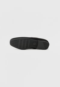 Schwarze Schuhsohle mit flachem Design, texturierten Rillen und kreisförmigem Markenlogo. Aus Gummi mit glatter Oberfläche gefertigt.
