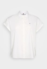 Chemise blanche à manches courtes avec col, dotée d'une fermeture à boutons à l'avant et d'un petit logo sur la poitrine. Tissu lisse, coupe ajustée.