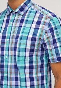 Kortärmad skjorta med rutigt mönster i nyanser av blått och grönt, med knappslå på kragen, två bröstfickor och ett lätt bomullstyg.