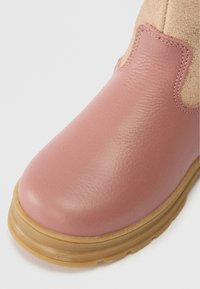 Ροζ δερμάτινη και μπεζ σουέτ μπότες με καφέ καουτσούκ σόλα, κοντινή λήψη στρογγυλής μύτης και πλευρικών ραφών στο λευκό φόντο.