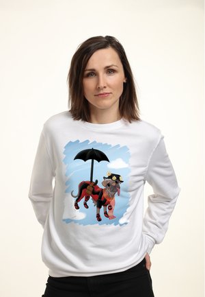 Kobieta o brązowych włosach do ramion ubrana w biały sweatshirt z nadrukiem kreskówkowego mopsika przebrane za Deadpoola z parasolem i kwiatami na kapeluszu.