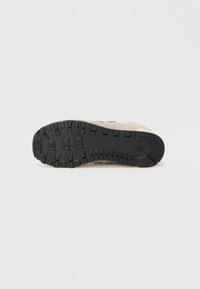 Semelle de chaussure avec un profil en caoutchouc noir présentant de profondes rainures et un dessus beige visible sur les bords, sur fond blanc uni.