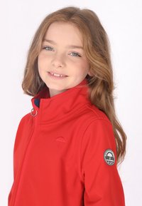 Rød softshell-jakke med høj krave, lynlåslukning og et paraplylogo på brystet og ærmet. Glat tekstur og skræddersyet pasform.