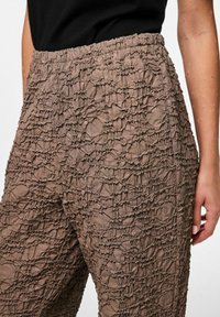 Smešani smeđi hlače s naboranim dizajnom i rastezljivim pojasom. Prikaz blizu pokazuje naboranu tkaninu s laganim sjajem.