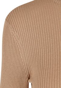 Gros plan sur un tissu en maille côtelée beige sur un vêtement à manches longues, montrant les détails des coutures d'épaule et de manche.