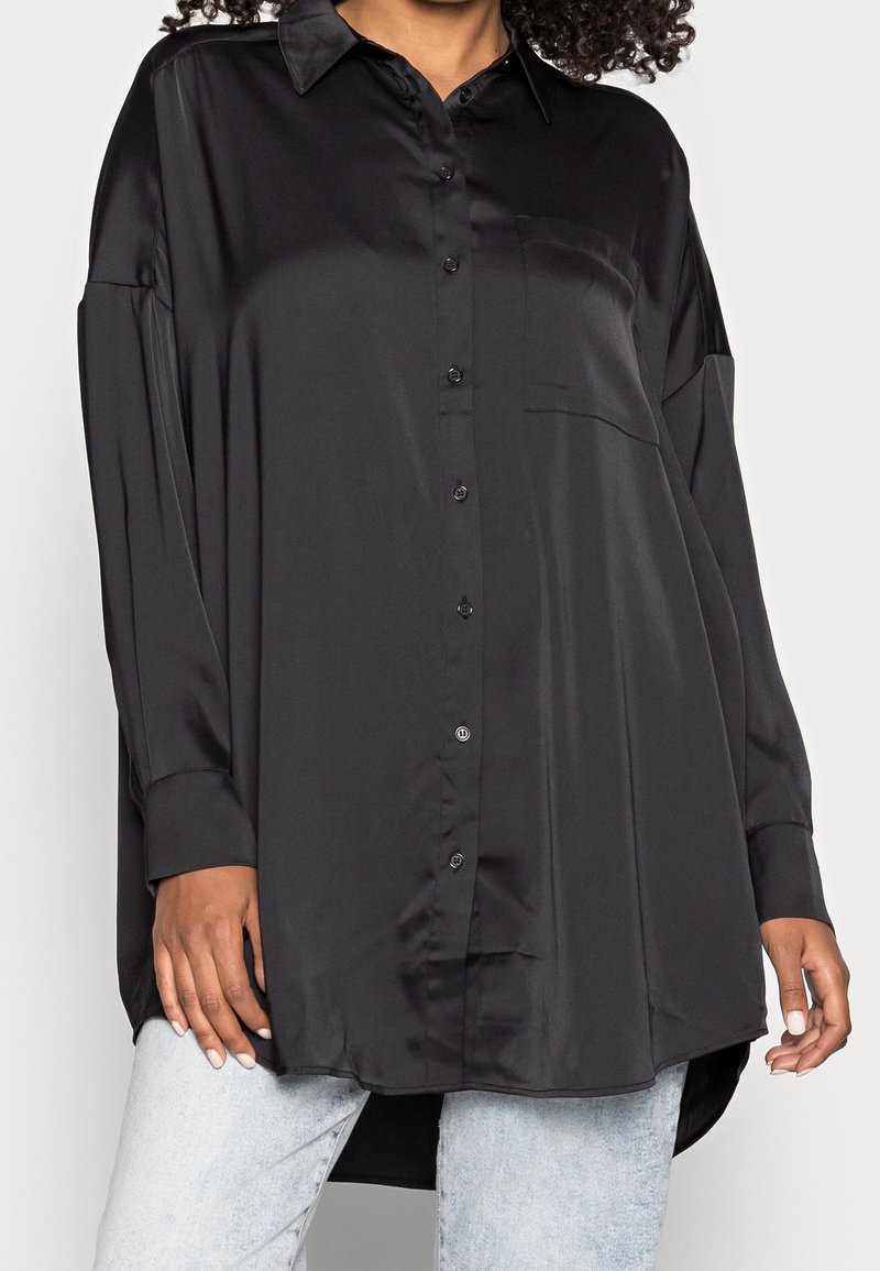 Camicia nera in satin con abbottonatura frontale, colletto a punta, maniche lunghe e taschino sul petto, con un orlo leggermente curvato e dal taglio ampio.