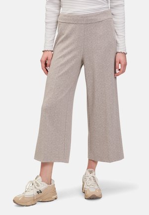 Hellbraune, strukturierte, weit geschnittene Hose mit flachem Bund, kombiniert mit beigen Sneakern. Längs gestreiftes Langarmshirt ist oben sichtbar.