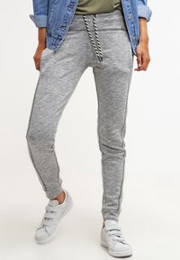 Grå sweatpants tillverkade av mjukt tyg, med snörning i midjan, slim fit och kontrasterande sidostripes. Kombinerat med vita sneakers.