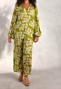 Completo floreale verde con una blusa ampia e pantaloni a gamba larga. Il tessuto sembra leggero, con maniche a sbuffo e scollatura a V.