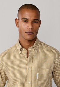 Camisa de cuadros de botones en amarillo y blanco. Presenta un cuello y un bolsillo en el pecho con una pequeña etiqueta. Tejido suave con un ajuste clásico.