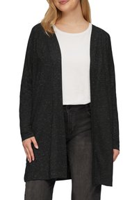 Schwarze offene Strickjacke mit einem strukturierten Muster, langen Ärmeln und lockerer Passform. Getragen über einem weißen Oberteil und kombiniert mit dunklen Jeans.