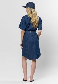 Džínová košeľová šaty s krátkymi rukávmi, opasok na páse a zakrivený spodok. Kombinované s čiapkou z rovnakého džínového materiálu a čiernymi sandálmi.