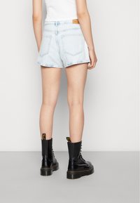 Světlé modré džíny s roztrhaným lemem a dvěma zadními kapsami. Spárovány s černými šněrovacími botami s žlutým poutkem.