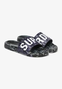 Zwarte en paarse camouflage slippers met een brede band waarop "SUPER" in witte tekst staat. Textuur van de voetbed en een vlakke zoolontwerp voor comfort.