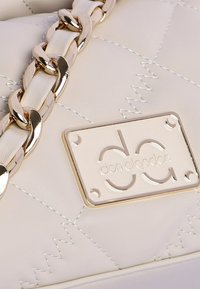 Bolso blanco acolchado con correa de cadena dorada, que presenta una placa de logo rectangular con el relieve "don algodón." Textura de cuero suave.