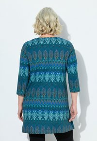 Tuerkisfarbige Tunika mit geometrischem Muster in Blau-, Braun- und Weißtönen, mit drei Viertelärmeln und einem runden Ausschnitt.