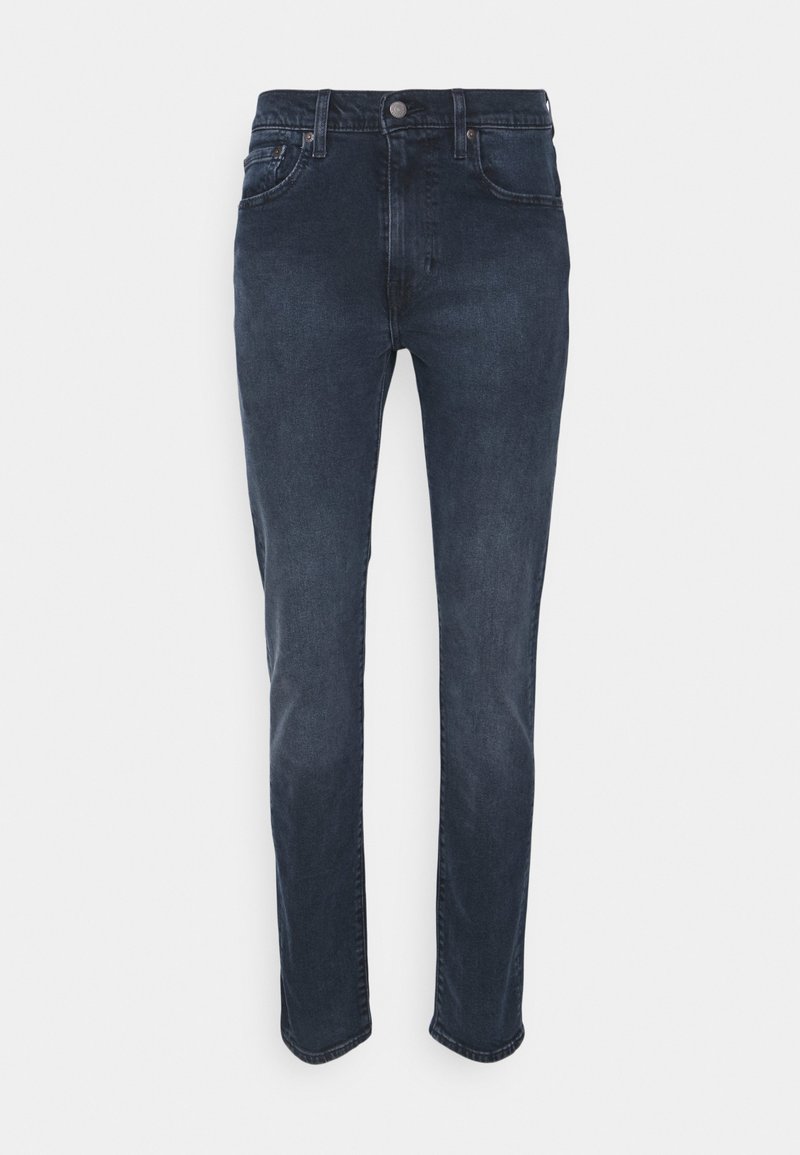 Jean en denim bleu foncé avec une coupe droite, cinq poches, fermeture par bouton et zip, et décoloration minimale. Texture lisse et design classique.