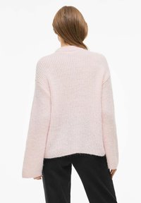 Jasnoróżowy, oversize sweter z prążkowaną fakturą, opuszczonymi ramionami i nieco dłuższym tylnym brzegiem. Miękki, dzianinowy materiał.