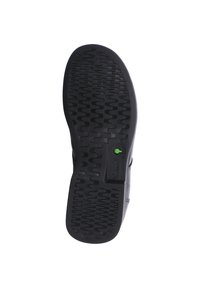 Schwarze Gummisohle mit strukturierten Mustern und einem grünen Akzent. Das Design umfasst Rillen für Traktion und Haltbarkeit.
