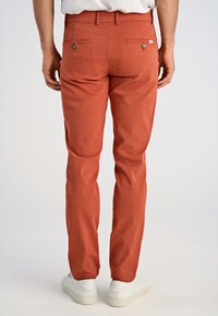 Męskie spodnie w kolorze rdzy o slim fit, z dwoma tylnymi kieszeniami zapinanymi na guzik oraz gładką, bawełnianą fakturą.