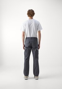 Grau Cargo-Hosen mit geradem Bein, mehreren Seitentaschen und einem Patch-Logo, kombiniert mit einem schlichten weißen T-Shirt und Sneakers.