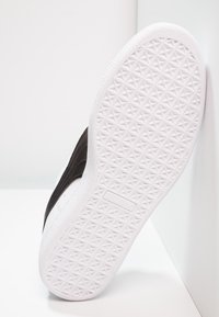 Baskets noires avec une semelle texturée, dotées d'une semelle extérieure en caoutchouc blanc et d'une tige en cuir noir lisse. Logo visible sur le côté.