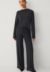 Schwarzes Pyjama-Set mit langen Ärmeln und weitem Bein, mit einem dezenten gesprenkelten Muster, weicher Textur und entspannter Passform.