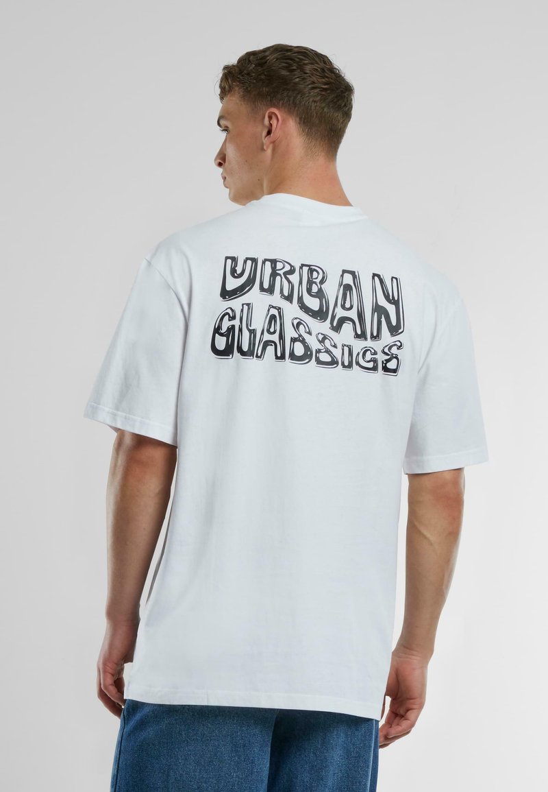 Balts kokvilnas t-krekls ar lielu melnbaltu grafisko tekstu uz muguras, kas lasāms "URBAN GLASSIGS." Brīvas formas un īsām piedurknēm.