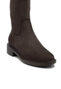 Botină din suede maro, până la genunchi, cu vârf rotunjit, toc pătrat și accente cusute, având o textură netedă și un design minimalist.