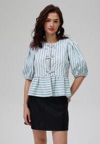 Gestreifte Peplum-Bluse in Hellgrün und Weiß, mit kurzen Puffärmeln, rundem Ausschnitt und dekorativen Schleifenakzenten auf der Vorderseite.