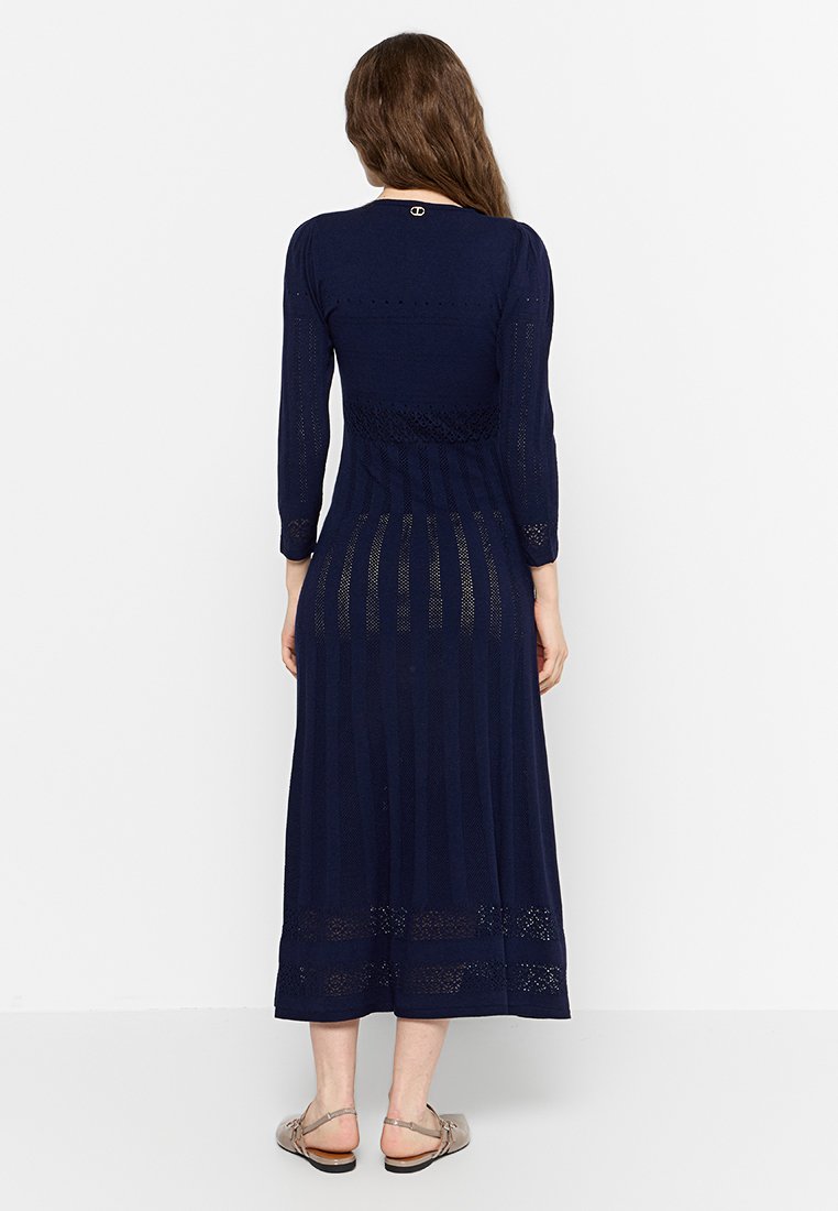 Robe maxi tricotée bleu marine avec des manches longues, présentant un motif texturé et des bandes transparentes le long de l'ourlet.
