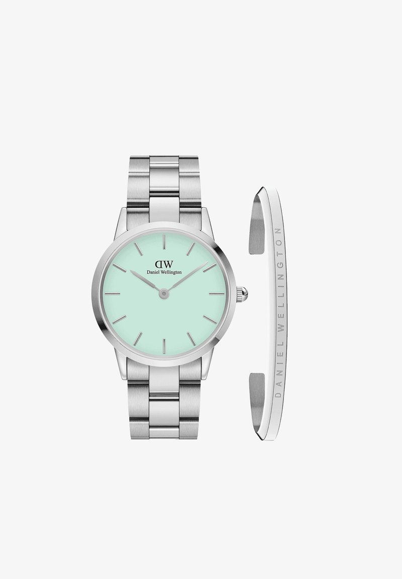 Sudraba nerūsējošā tērauda pulkstenis ar piparmētru zaļu ciparnīcu, kas aprīkots ar minimālistiskiem stundu rādītājiem un rādītājiem. Ietverts atsevišķs gravēts sudraba rokassprādze.