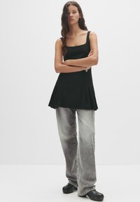 Top nero senza maniche con scollatura quadrata e design plissettato, abbinato a jeans grigi a gamba ampia e scarpe con zeppa.