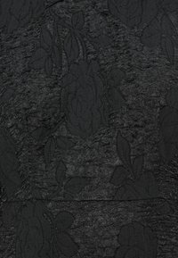 Juodas tekstūruotas audinys su gėlių raštu ir pakeltu detalėmis. Lygūs plotai prieštarauja šiek tiek susigūžusiai dangai. Matomų metalinių detalių nėra.