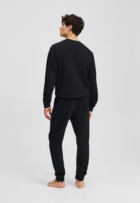 Set de hanorac și pantaloni de trening negri, cu guler rotund, manșete ribbate și croială lejeră. Fabricat dintr-un material texturat și moale.