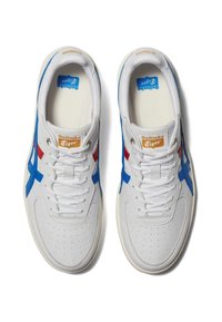 Białe sneakersy z niebieskimi i czerwonymi akcentami, perforowanym noskiem, płaskimi sznurówkami i wyściełanym kołnierzem. Zawierają logo Onitsuka Tiger na języku.