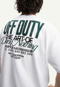 White cotton t-shirt with a large green graphic print on the back, featuring text about leisure and a contact number in black font.