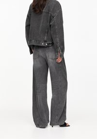 Chaqueta de denim gris, de corte oversize, con cierre de botones y aberturas laterales. Combinada con pantalones de denim gris de talle alto y pierna ancha.