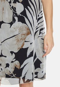Blumenkleid aus leichtem Stoff mit einem grau-weißen Design, akzentuiert mit Braun. Der Saum ist leicht transparent und zeigt geschichtete Texturen.