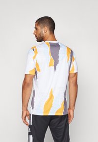Maglietta atletica bianca a maniche corte con motivi astratti in grigio, giallo e blu. Tessuto liscio con un design a collare tondo.