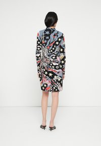 Šaty s dlhým rukávom s farebným vzorom obsahujúcim tigre, hviezdy a abstraktné tvary v čiernych, modrých, červených a ružových tónoch.